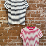 Two striped t-shirts hanging on wooden hangers against a brick wall.