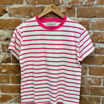 Pink and white striped t-shirt on a wooden hanger against a brick wall.