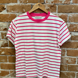 Pink and white striped t-shirt on a wooden hanger against a brick wall.