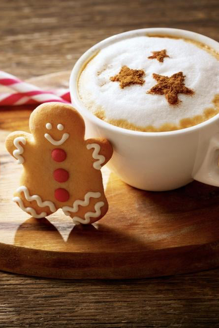White mug with a festive drink and gingerbread cookies on a wooden surface