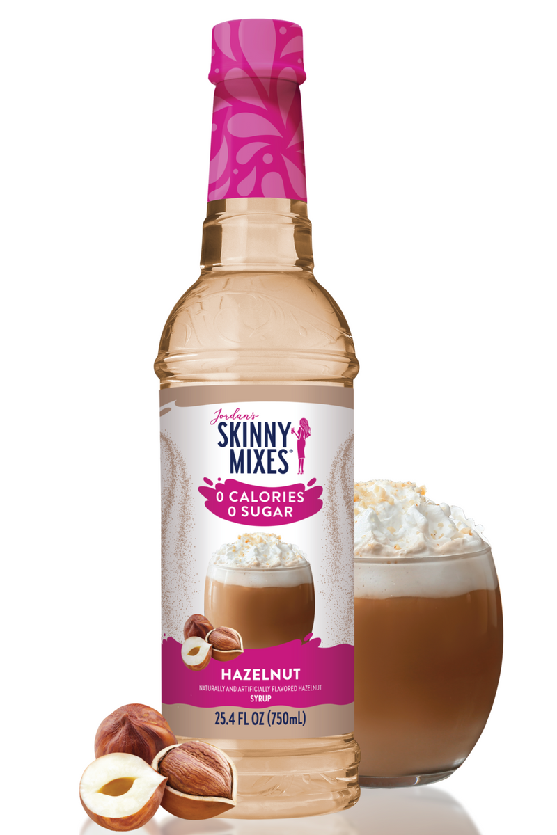 Bottle of Skinny Mixes Hazelnut syrup with a glass of hazelnut-flavored drink and nuts on a white background
