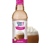 Bottle of Skinny Mixes Hazelnut syrup with a glass of hazelnut-flavored drink and nuts on a white background