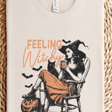 Beige t-shirt with 'Feeling Witchy' graphic design on a woven surface
