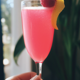 Pink cocktail in a glass with a lemon twist and raspberry, held by a hand, with a blurred indoor background.