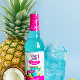 Bottle of Sunny Mixes Caipirinha Mix with a pineapple, coconut, and blue cocktail on a light blue background