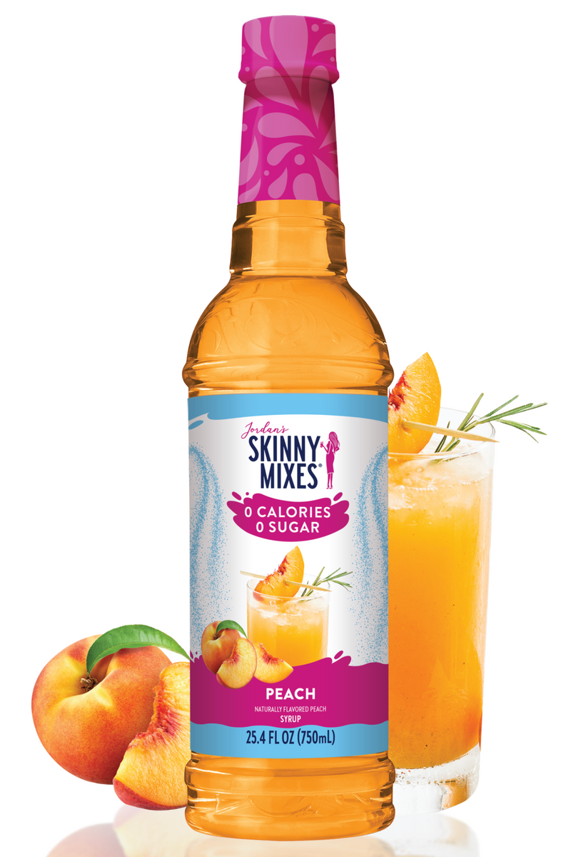 Skinny Mixes peach syrup bottle with a glass of peach juice and peaches on a white background