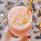 Pink cocktail with gold glitter and a straw held by a hand against a festive background.