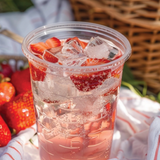 Strawberry iced drink in a clear cup with a picnic setting featuring strawberries and a basket.