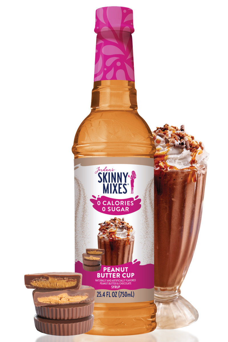 Skinny Mixes Peanut Butter Cup syrup bottle with a glass of dessert and smaller cups on a white background