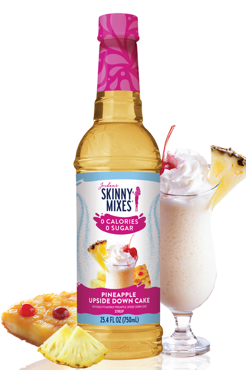 Bottle of Skinny Mixes Pineapple Upside Down Cake syrup with a glass of milkshake and pineapple slices on a white background