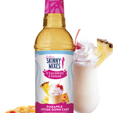 Bottle of Skinny Mixes Pineapple Upside Down Cake syrup with a glass of milkshake and pineapple slices on a white background