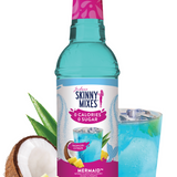 Bottle of Skinny Mixes Mermaid syrup with a glass of blue drink, pineapple, and coconut on a white background