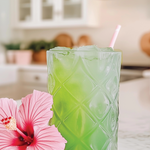 Green cocktail in a textured glass with a pink flower on a kitchen counter