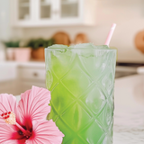 Green cocktail in a textured glass with a pink flower on a kitchen counter