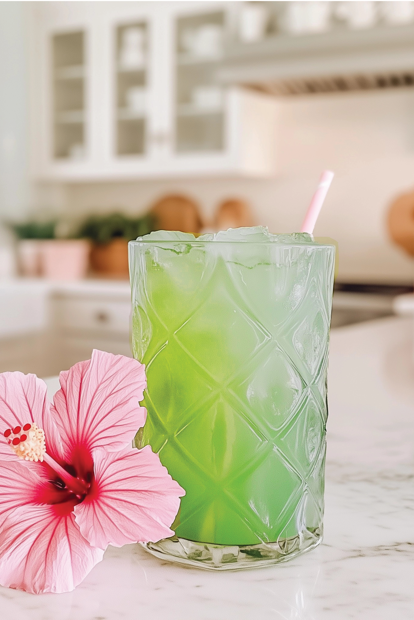 Green cocktail in a textured glass with a pink flower on a kitchen counter