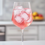 Pink cocktail with ice in a wine glass on a kitchen counter