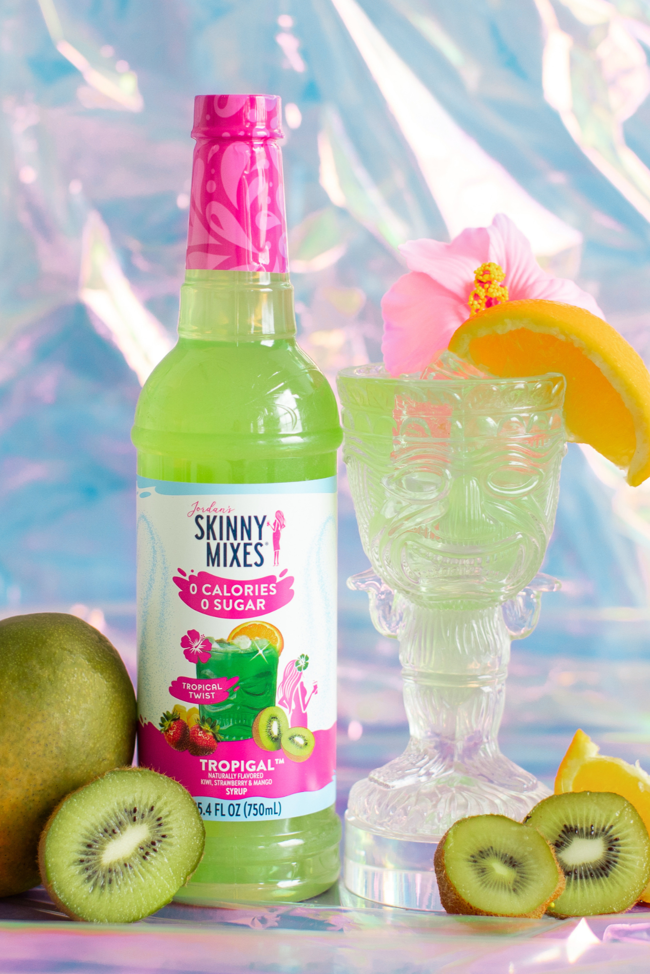 Bottle of Skinny Mixes Tropigenic drink with a glass, fruit, and colorful background