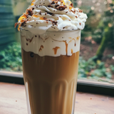 Cappuccino with whipped cream and chocolate shavings on a wooden table with a window in the background.