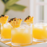 Three glasses of orange juice with pineapple slices on a white tray.