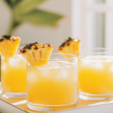 Three glasses of orange juice with pineapple slices on a white tray.