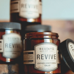Multiple bottles of Revive Leather Conditioning Cream with brown labels on a wooden surface, with the primary bottle in the foreground.